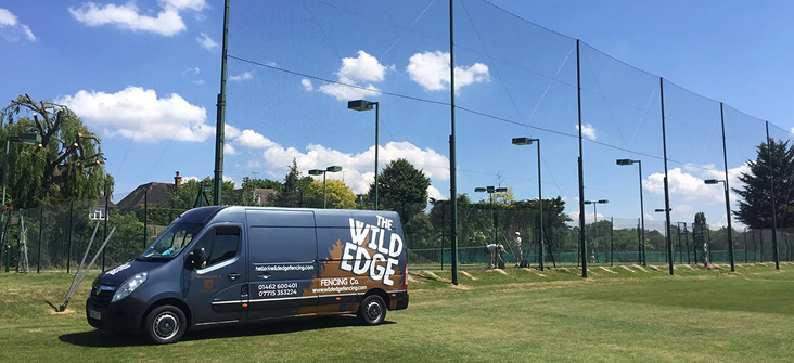 Wild Edge Fencing van beside tall perimeter netting around outdoor sports courts
